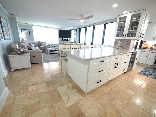 kitchen featuring stone tile floors, glass insert cabinets, open floor plan, a kitchen bar, and white cabinetry