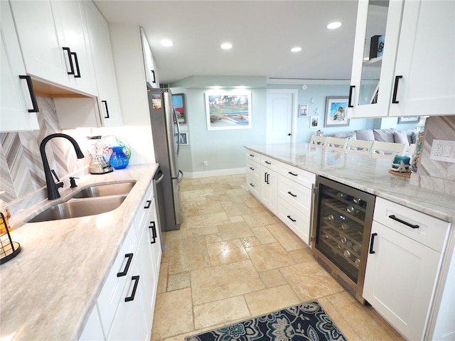 kitchen with wine cooler, a sink, white cabinetry, freestanding refrigerator, and stone tile flooring