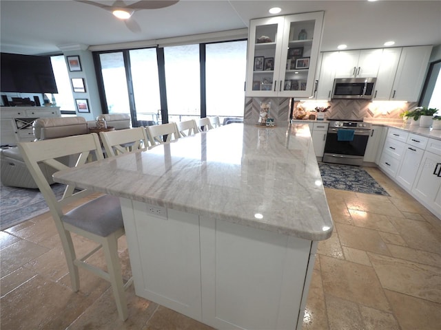 kitchen featuring light stone counters, a breakfast bar, stone tile floors, decorative backsplash, and appliances with stainless steel finishes