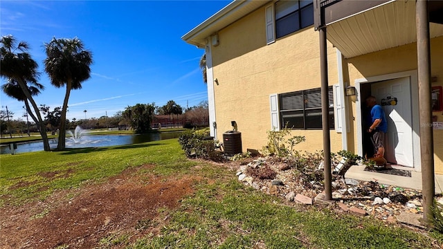 view of side of home with a water view, central air condition unit, a lawn, and stucco siding