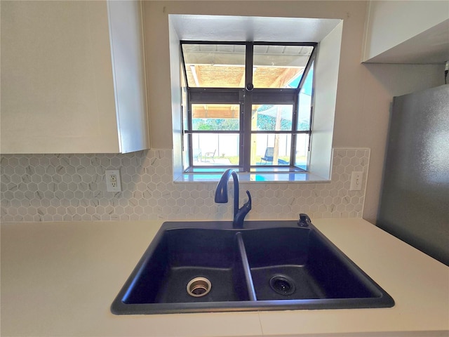 kitchen with light countertops, white cabinets, a sink, and backsplash