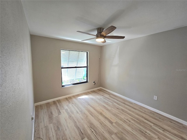 spare room featuring a textured wall, light wood-type flooring, ceiling fan, and baseboards