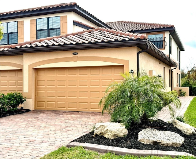 view of front of house with stucco siding, decorative driveway, a garage, and a tile roof