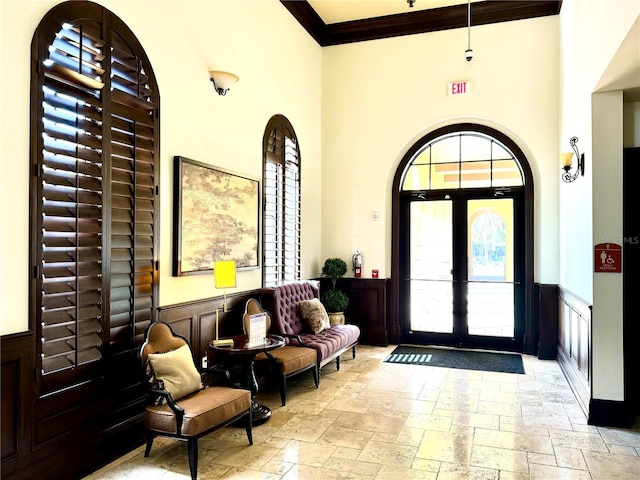 foyer with wainscoting, stone tile floors, a high ceiling, and french doors