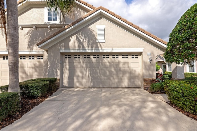 view of front facade with a garage, a tile roof, concrete driveway, and stucco siding