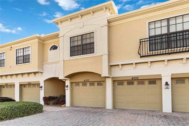 view of front of property with driveway, an attached garage, a balcony, and stucco siding