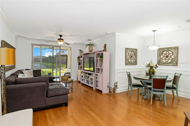 living area with a decorative wall, wood finished floors, a ceiling fan, wainscoting, and crown molding