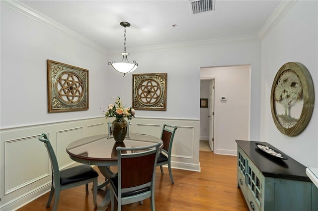 dining space with a wainscoted wall, ornamental molding, wood finished floors, and visible vents