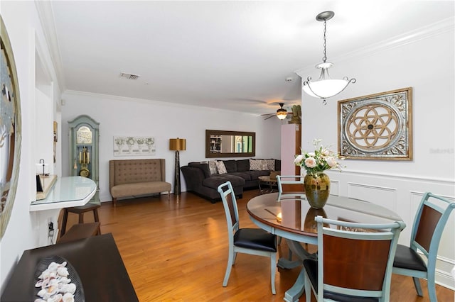 dining room with light wood finished floors, a decorative wall, visible vents, and crown molding