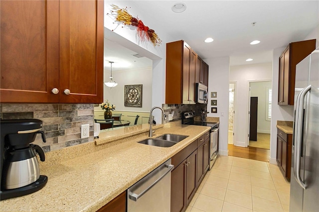 kitchen with appliances with stainless steel finishes, light stone counters, a sink, backsplash, and light tile patterned flooring