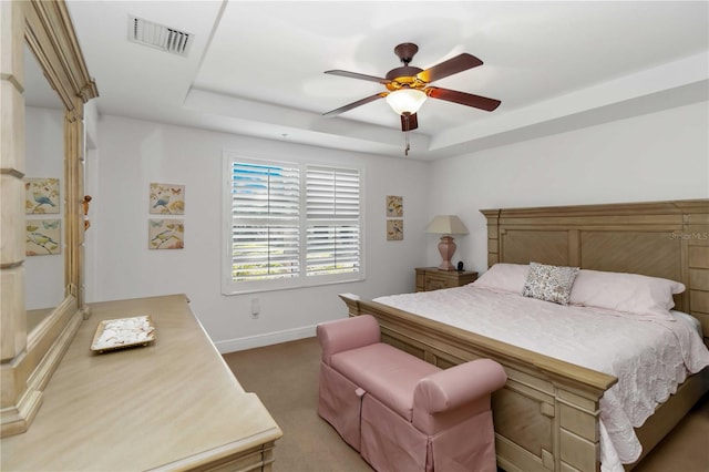 carpeted bedroom with a ceiling fan, a raised ceiling, visible vents, and baseboards