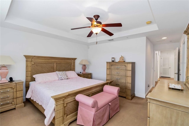 bedroom featuring light carpet, visible vents, baseboards, a raised ceiling, and ceiling fan