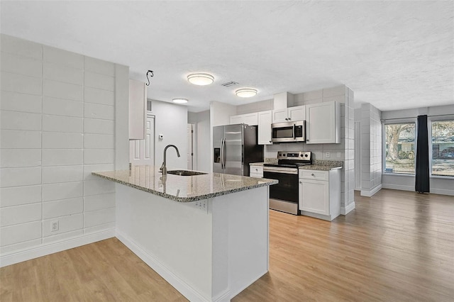 kitchen with a peninsula, stainless steel appliances, stone counters, white cabinetry, and a sink