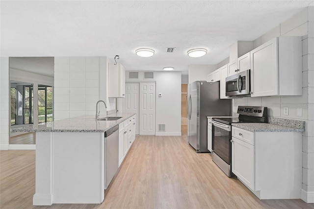 kitchen with white cabinets, light stone countertops, stainless steel appliances, and a sink