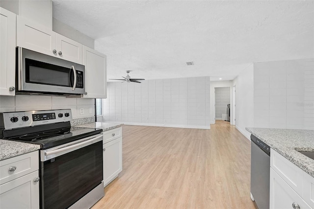 kitchen with appliances with stainless steel finishes, light wood-style floors, light stone countertops, and white cabinets