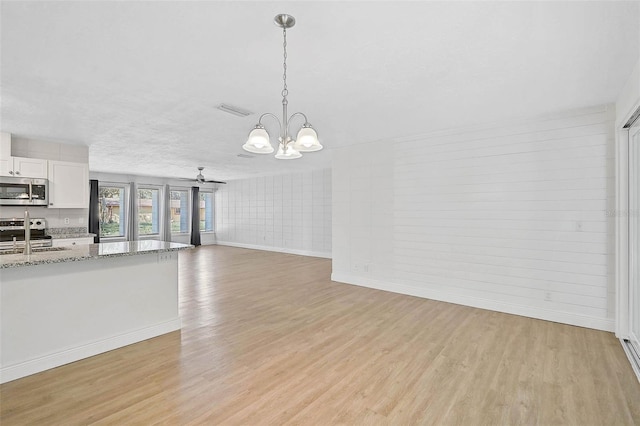 unfurnished living room with visible vents, a sink, light wood-type flooring, baseboards, and ceiling fan with notable chandelier