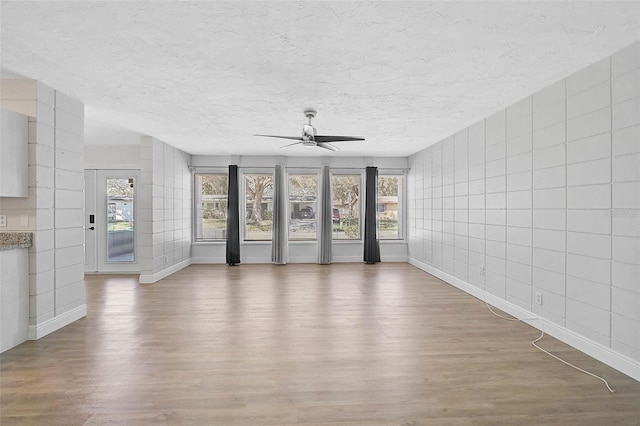 unfurnished living room featuring a textured ceiling, wood finished floors, tile walls, baseboards, and a ceiling fan