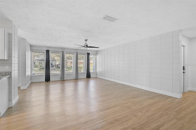 unfurnished living room featuring baseboards, visible vents, ceiling fan, a textured ceiling, and light wood-type flooring