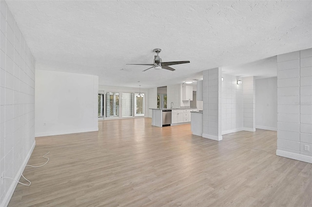 unfurnished living room with light wood-style flooring, a textured ceiling, tile walls, and a ceiling fan