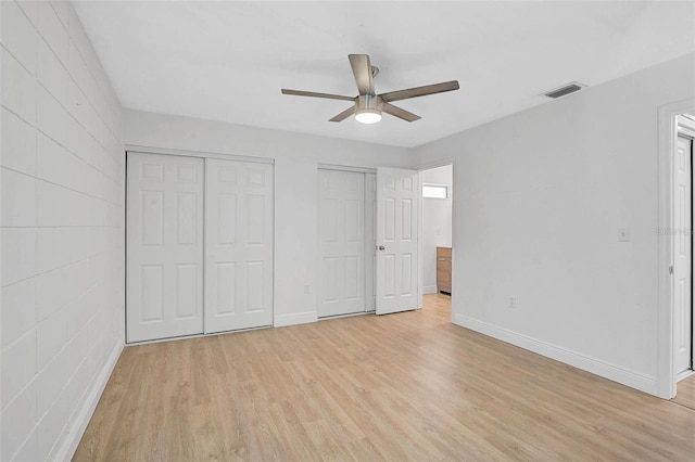 unfurnished bedroom featuring ceiling fan, light wood-style flooring, visible vents, baseboards, and multiple closets