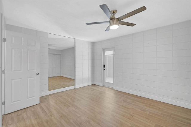 unfurnished bedroom with tile walls, light wood finished floors, a closet, a ceiling fan, and baseboards