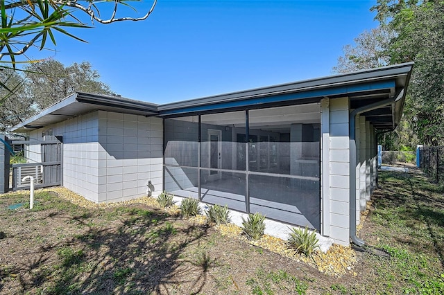 view of side of home with a sunroom, fence, and concrete block siding