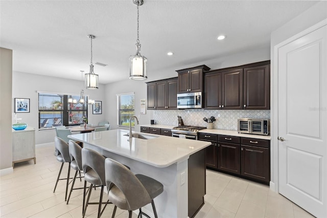 kitchen with a breakfast bar area, tasteful backsplash, appliances with stainless steel finishes, a sink, and an island with sink