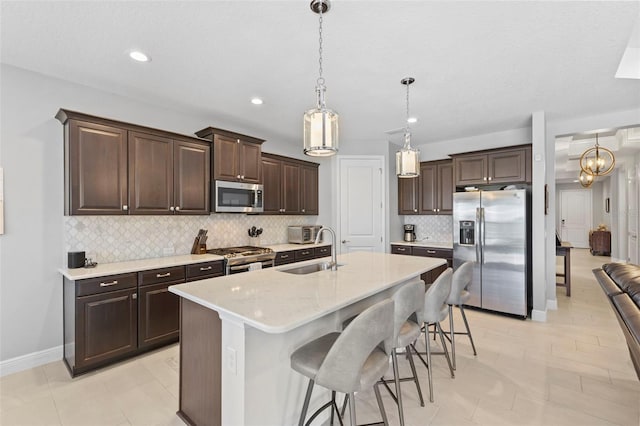 kitchen featuring appliances with stainless steel finishes, a kitchen island with sink, a sink, dark brown cabinetry, and a kitchen bar