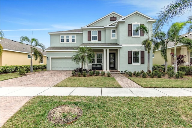 traditional-style home featuring an attached garage, a front yard, decorative driveway, and stucco siding