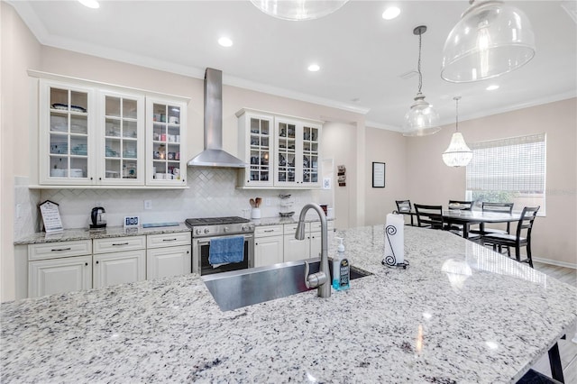 kitchen featuring a sink, wall chimney range hood, backsplash, gas stove, and crown molding