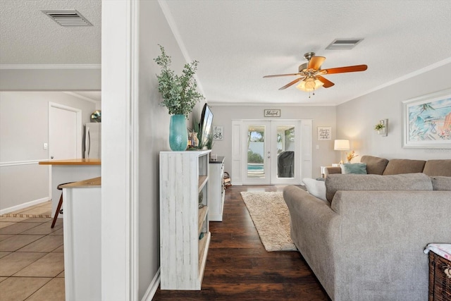 living room featuring a textured ceiling, french doors, ornamental molding, and visible vents