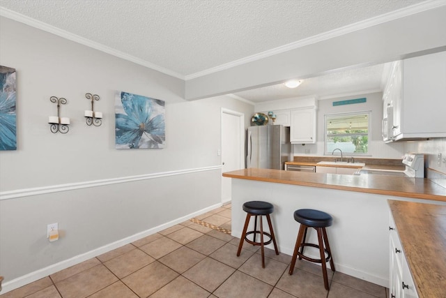 kitchen featuring a breakfast bar area, stainless steel appliances, a peninsula, white cabinets, and wooden counters