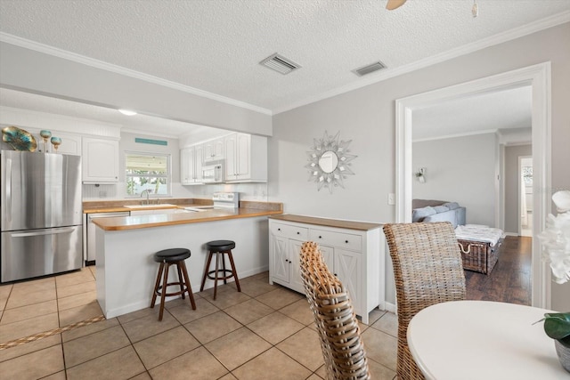 kitchen featuring visible vents, white cabinets, a kitchen breakfast bar, freestanding refrigerator, and a peninsula