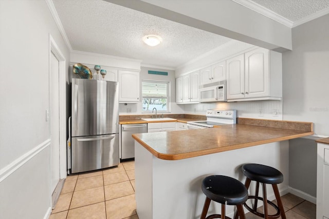 kitchen with a breakfast bar, stainless steel appliances, white cabinets, a sink, and a peninsula