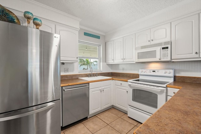 kitchen with light tile patterned floors, a sink, white cabinetry, ornamental molding, and appliances with stainless steel finishes