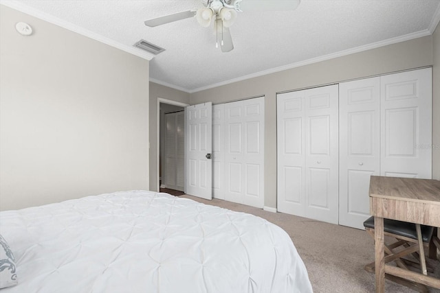 bedroom featuring visible vents, ornamental molding, carpet, a textured ceiling, and multiple closets