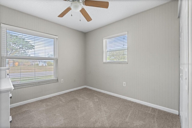 empty room with light carpet, ceiling fan, baseboards, and a textured ceiling