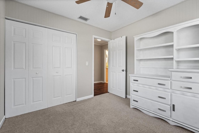 unfurnished bedroom with a textured ceiling, light carpet, visible vents, a ceiling fan, and a closet