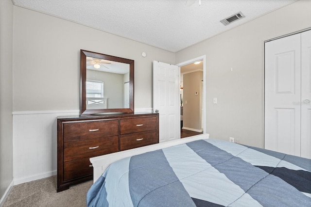 bedroom featuring visible vents, light colored carpet, a wainscoted wall, a textured ceiling, and a closet