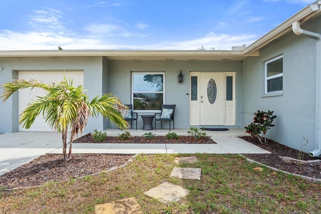 entrance to property featuring an attached garage, a porch, concrete driveway, and stucco siding