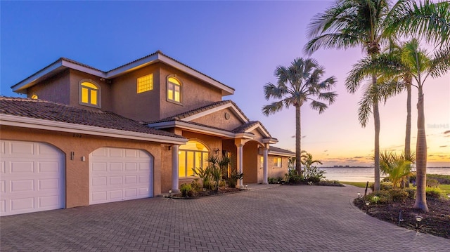 view of front of property featuring an attached garage, decorative driveway, a water view, and stucco siding