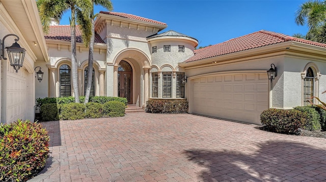 mediterranean / spanish-style house featuring decorative driveway, a tiled roof, an attached garage, and stucco siding