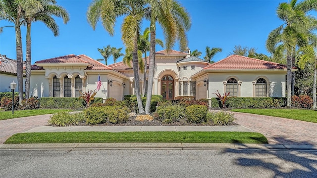 mediterranean / spanish home with a garage, decorative driveway, a tile roof, and stucco siding