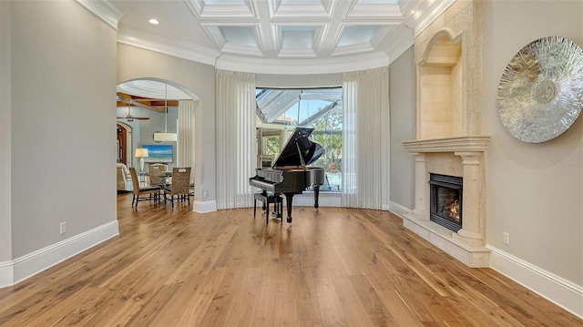 living area with baseboards, coffered ceiling, ornamental molding, wood finished floors, and a fireplace