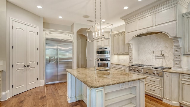 kitchen with light wood-style flooring, stainless steel appliances, cream cabinetry, light stone countertops, and open shelves