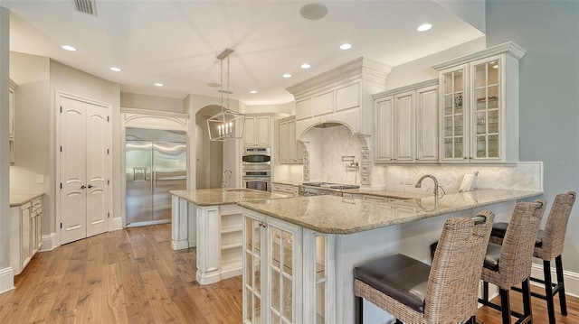 kitchen with a peninsula, visible vents, appliances with stainless steel finishes, light wood finished floors, and tasteful backsplash