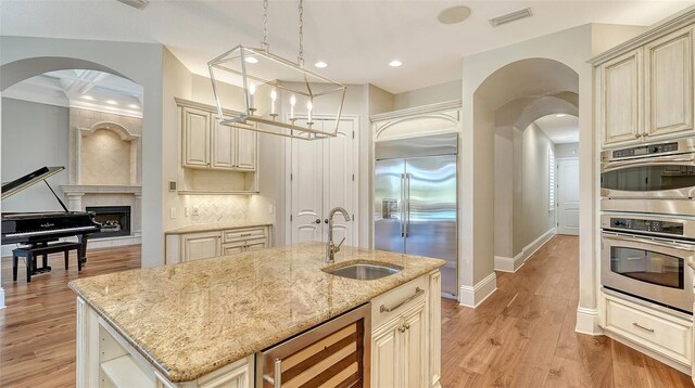 kitchen featuring beverage cooler, appliances with stainless steel finishes, light stone countertops, cream cabinets, and a sink