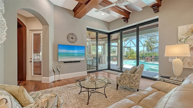 living room featuring ceiling fan, wood finished floors, a sunroom, baseboards, and beam ceiling