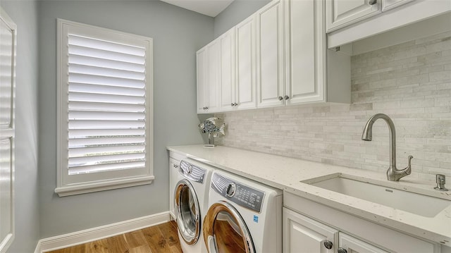 laundry area featuring cabinet space, baseboards, wood finished floors, independent washer and dryer, and a sink