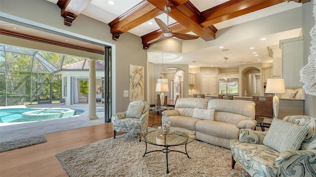 living area featuring arched walkways, a towering ceiling, beamed ceiling, light wood-style floors, and recessed lighting